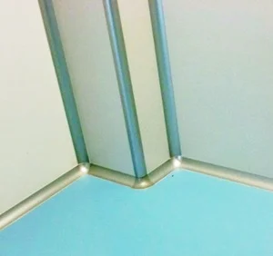 Acessórios cantos arredondados para Sala Limpa, Imagem de coluna revestida com divisórias e a acabadas com canto arredondado para salalimpa em alumínio anodizado nos encontros das paredes e conchas e o piso epoxy em tom de azul claro.