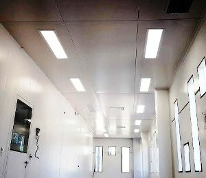 Área extensa com paredes divisórias e forro iluminado por luminárias para sala limpa, com lâmpadas de LED. Instaladas em série.
