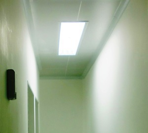 Corredor em alvenaria com pintura clara destacando na imagem a ilumnção de uma luminária enbutida no forro e os cantos arredondados do teto.