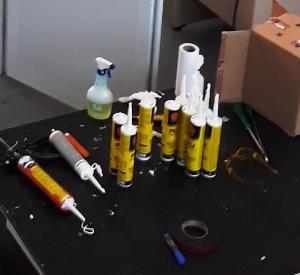 bancada com diversos selantes em silicone para sala limpa e os acessórios para aplicação expostos, compõem a imagem.